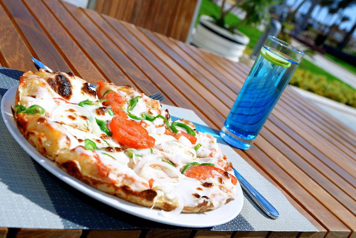 Eine Pizza auf einem Holztisch mit einem Glas blauem Getränk.