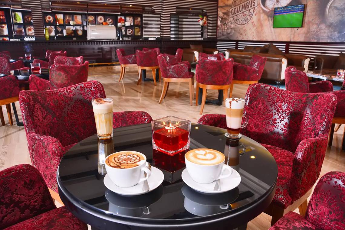 Loungebereich des Pickalbatros Royal Moderna Resort mit rot gepolsterten Stühlen und Kaffeespezialitäten auf dem Tisch.