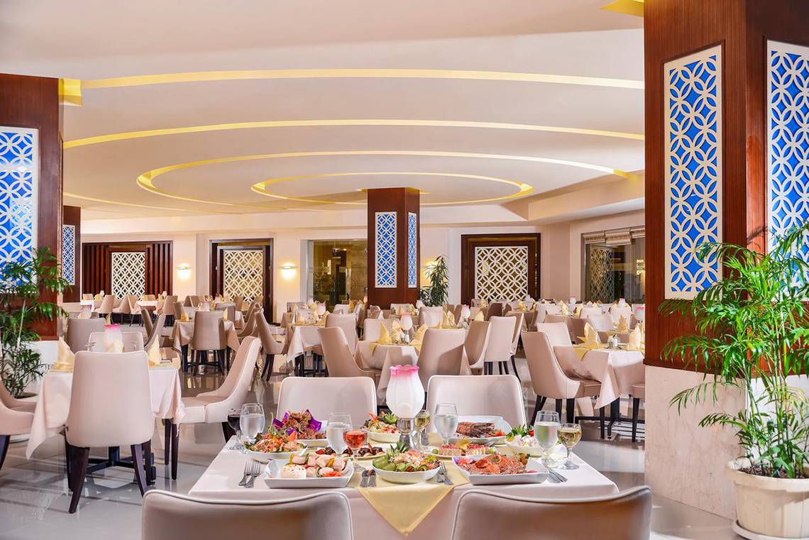 Innenansicht des Restaurants im Pickalbatros Royal Moderna Resort mit gedeckten Tischen und Pflanzen.