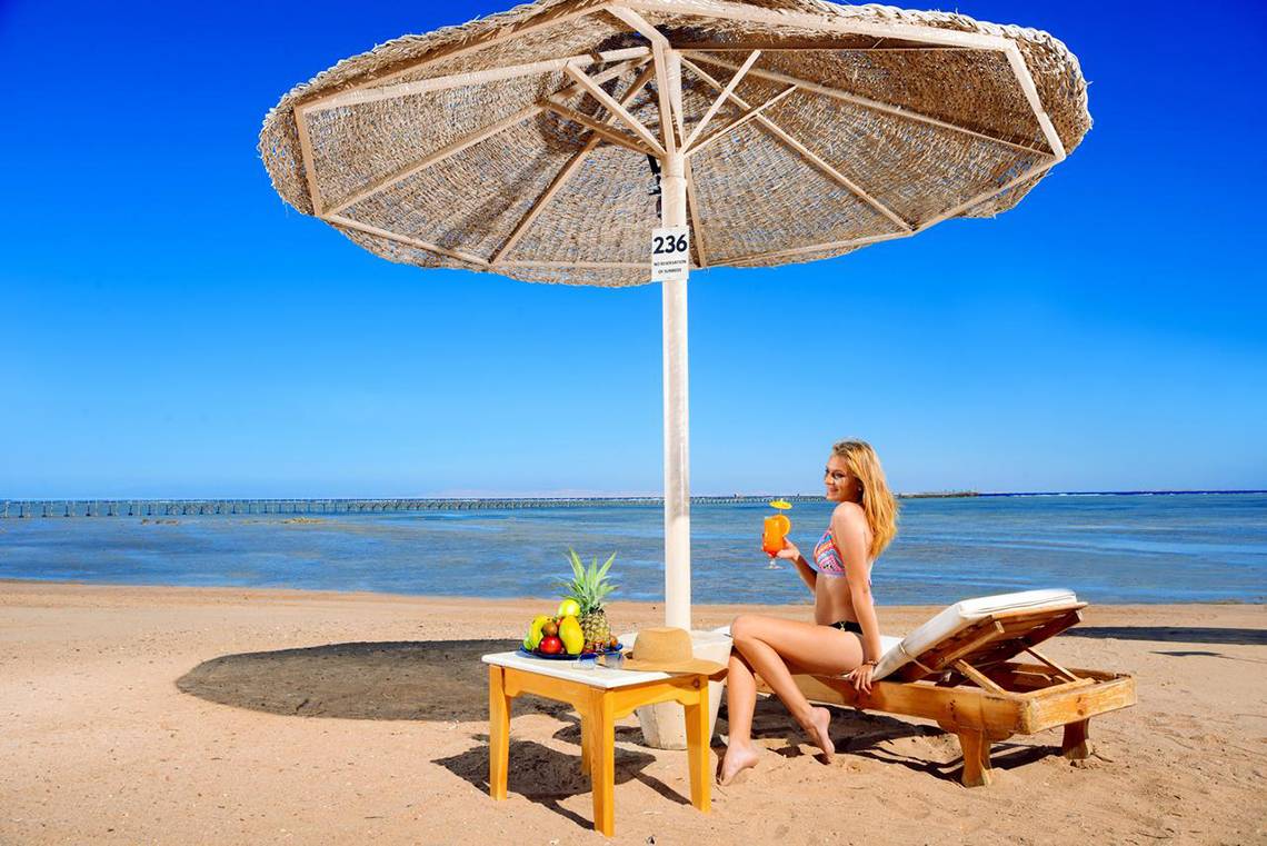 Eine Frau sitzt unter einem Sonnenschirm am Strand und genießt ein Getränk und Obst.
