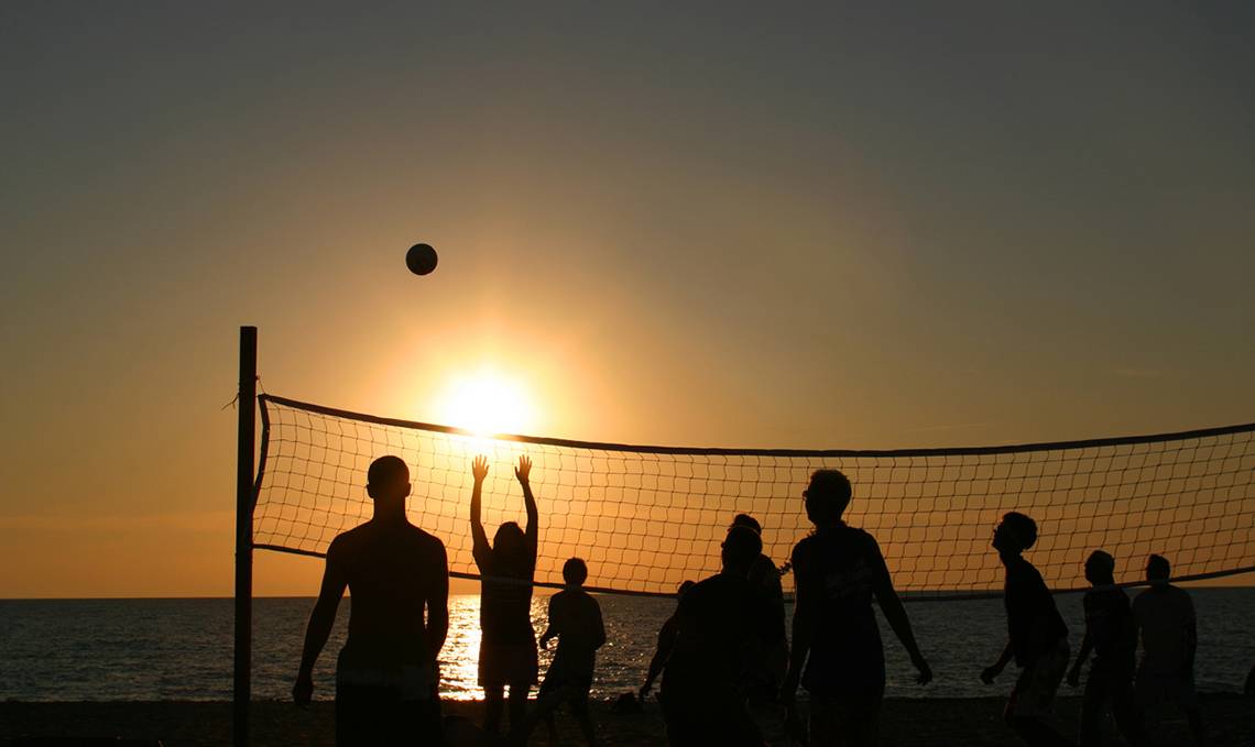 Gruppe von Menschen spielt Volleyball am Strand während des Sonnenuntergangs.