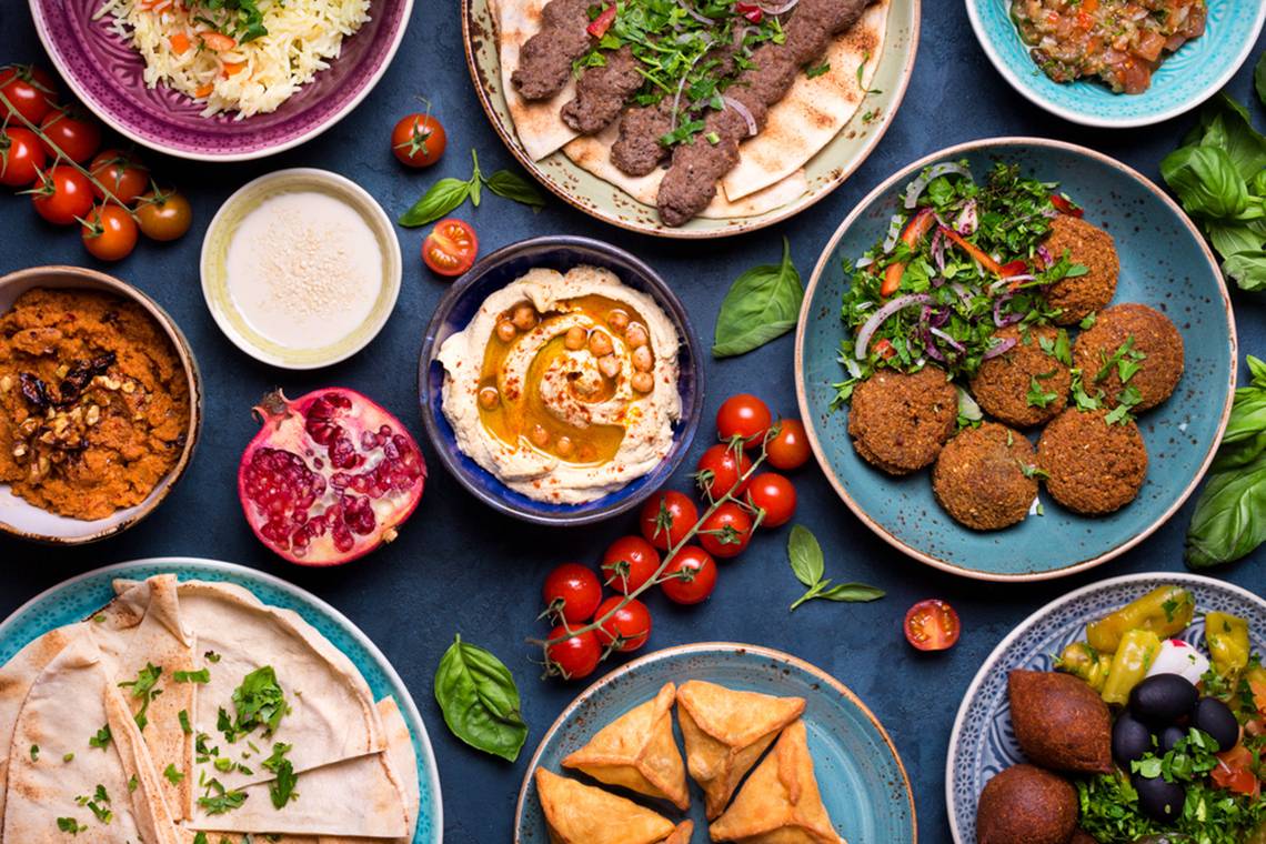 Orientalische Gerichte wie Falafel, Hummus und verschiedene Salate auf einem blauen Hintergrund.
