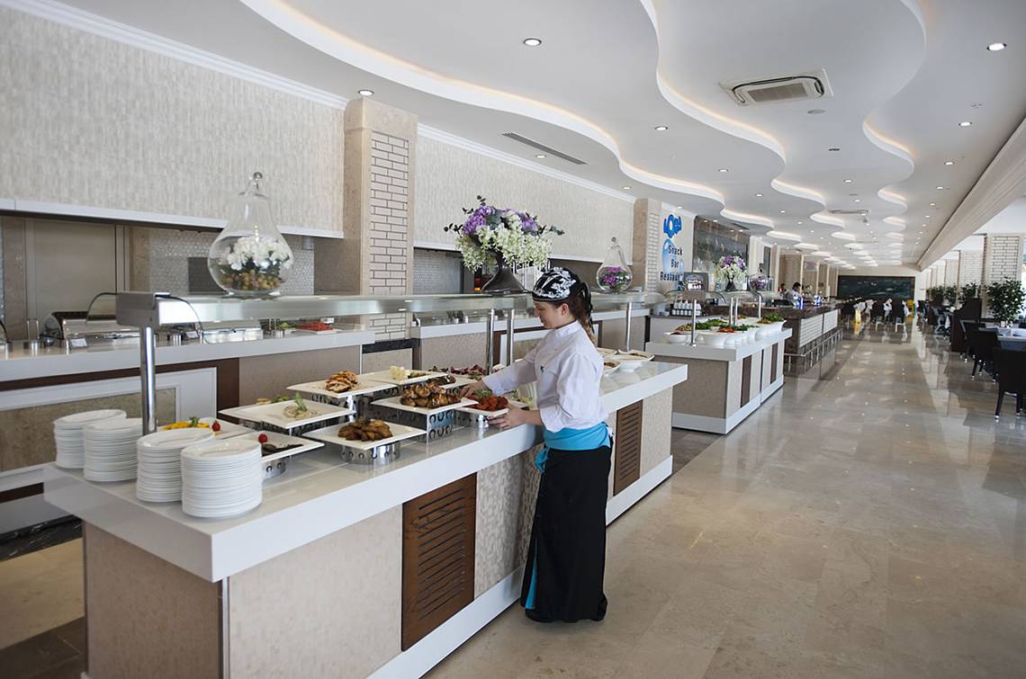 Ein Buffet-Tisch im Hotelrestaurant Crystal Waterworld Aqua Collection mit verschiedenen Gerichten und einer Serviererin.