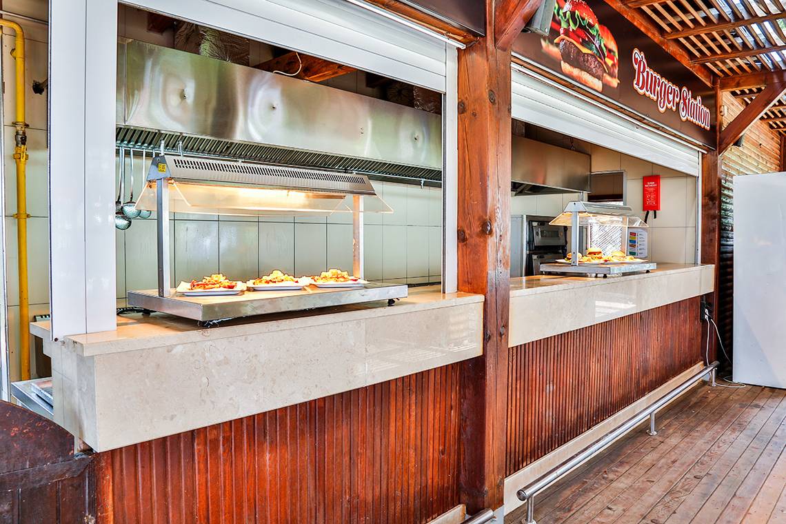 Innenbereich der Burger Station mit Speisen auf Warmhaltetischen und Holzwänden.
