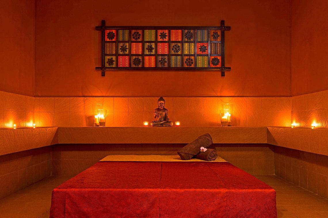 Spa-Zimmer im Le Meridien Abu Dhabi mit Buddha-Statue, Kerzen und rotem Bett.