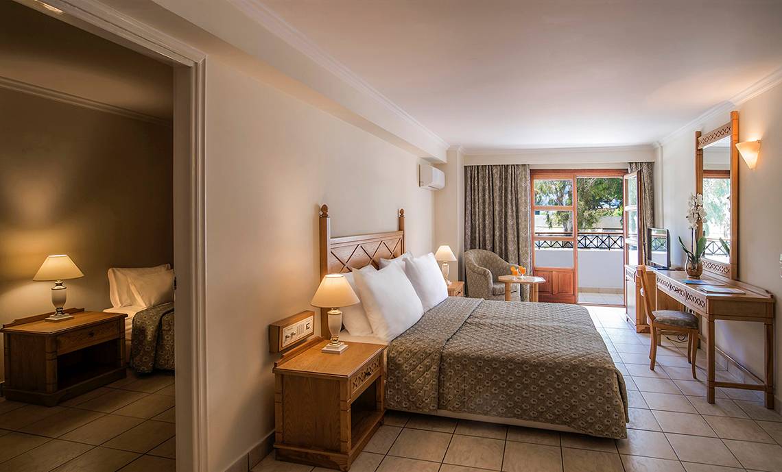 Schlafzimmer im Mitsis Petit Palais Beach Hotel mit Bett, Schreibtisch und Balkon.