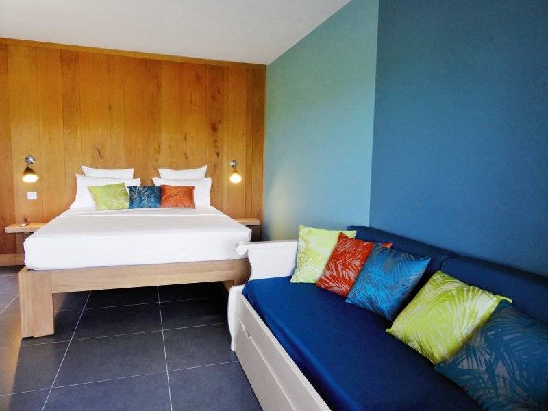 Schlafzimmer im Aparthotel Le Panoramic mit blauer Wand, Holzbett und Sofa.