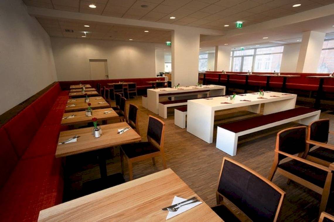 Restaurantbereich des Zeitgeist Vienna Hauptbahnhof mit roten Bänken und Holztischen.