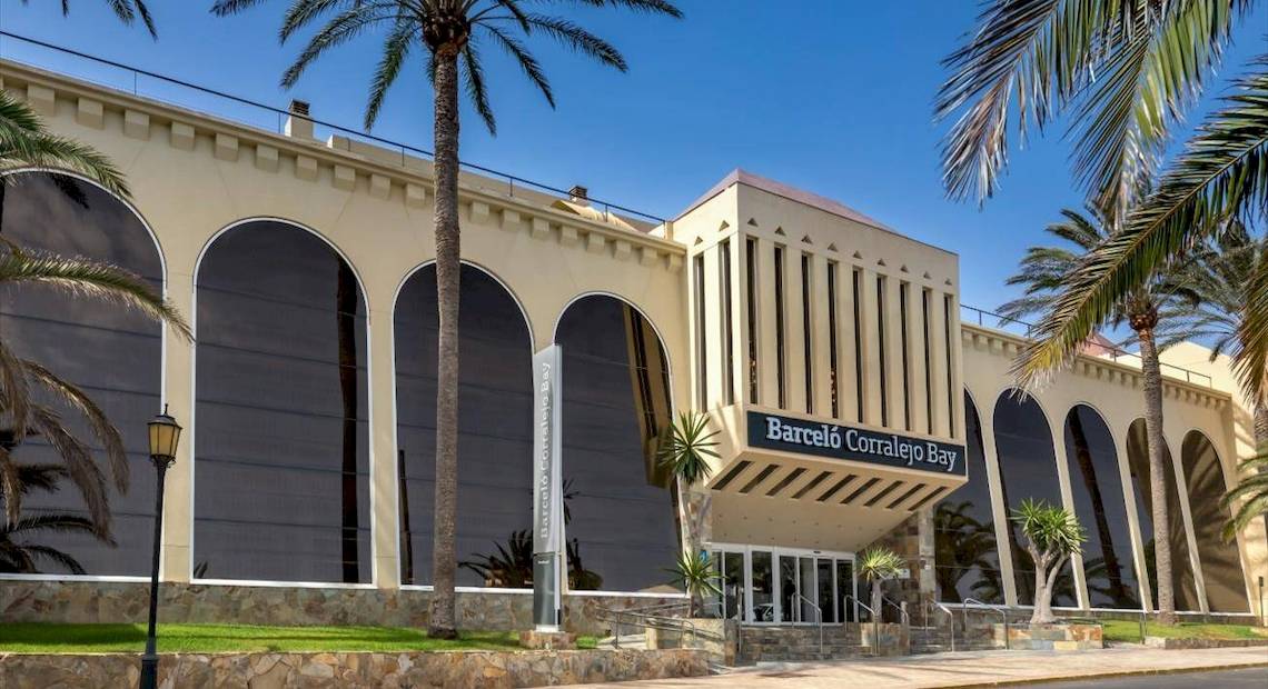 Außenansicht des Barcelo Corralejo Bay Hotels mit Palmen und bogenförmigen Fenstern.