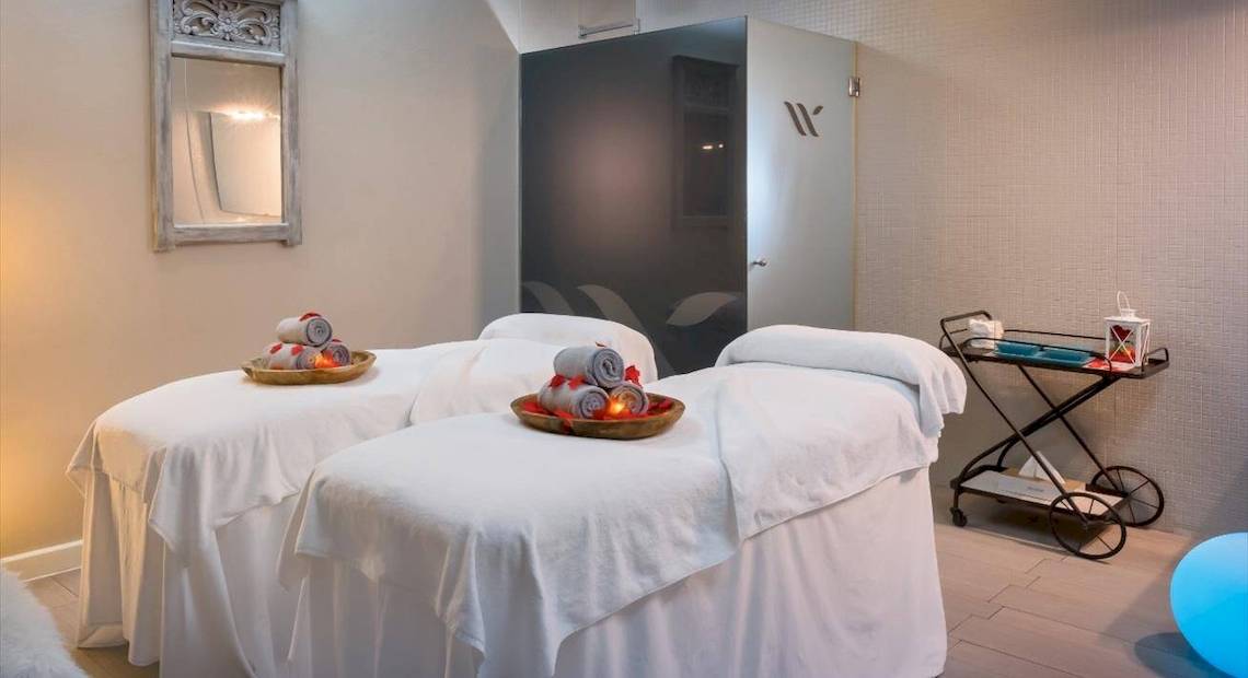Massageraum im Barcelo Corralejo Bay Hotel mit zwei Massagetischen, Kissen und Kerzen.