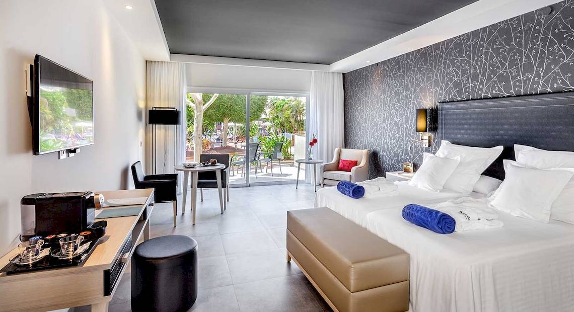 Hotelzimmer des Barcelo Corralejo Bay mit Doppelbetten, Fernseher und Terrasse.