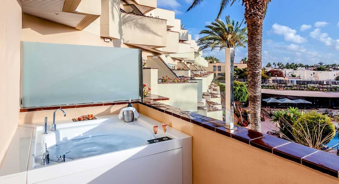 Balkon mit Whirlpool im Barcelo Corralejo Bay Hotel mit Blick auf Palmen und Gebäude.