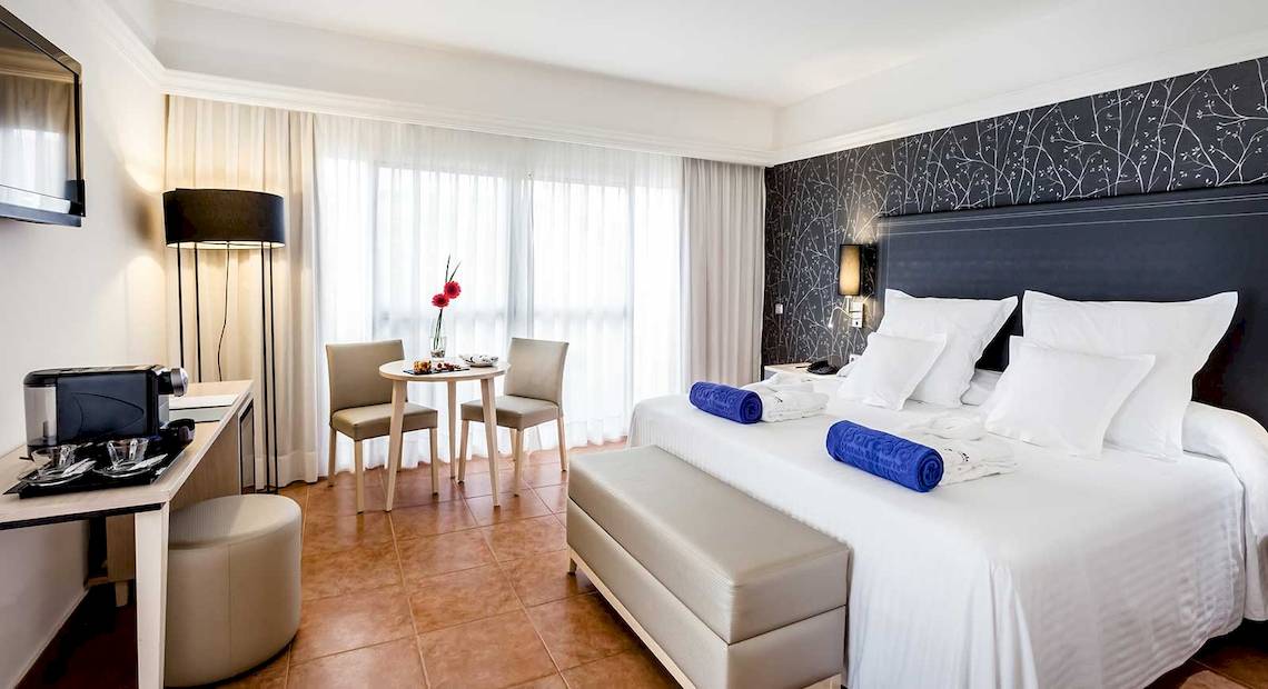 Zimmer im Barcelo Corralejo Bay Hotel mit Bett, Tisch, Stühlen und Dekor.