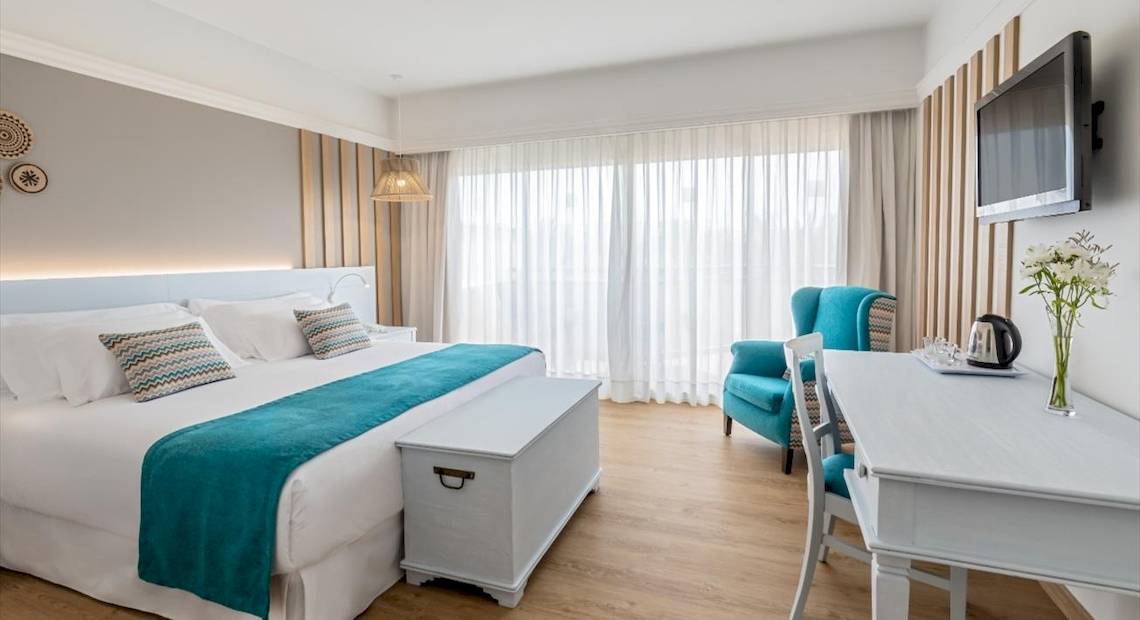 Innenansicht eines Hotelzimmers mit Bett, Kissen, Tisch, Stuhl und Fernseher.