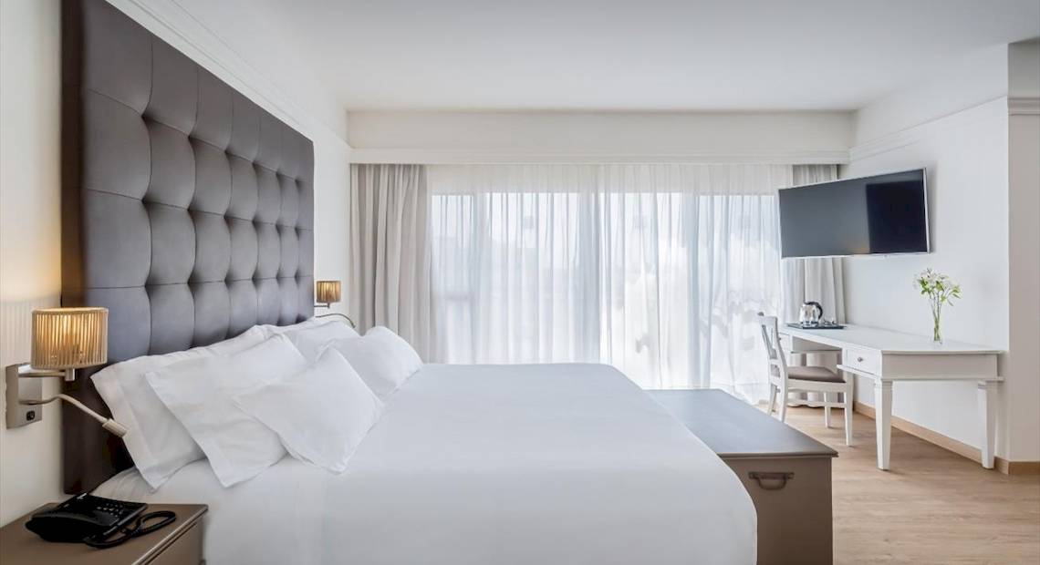 Hotelzimmer im Barcelo Corralejo Bay mit einem großen Bett, einem Schreibtisch und einem Fernseher an der Wand.
