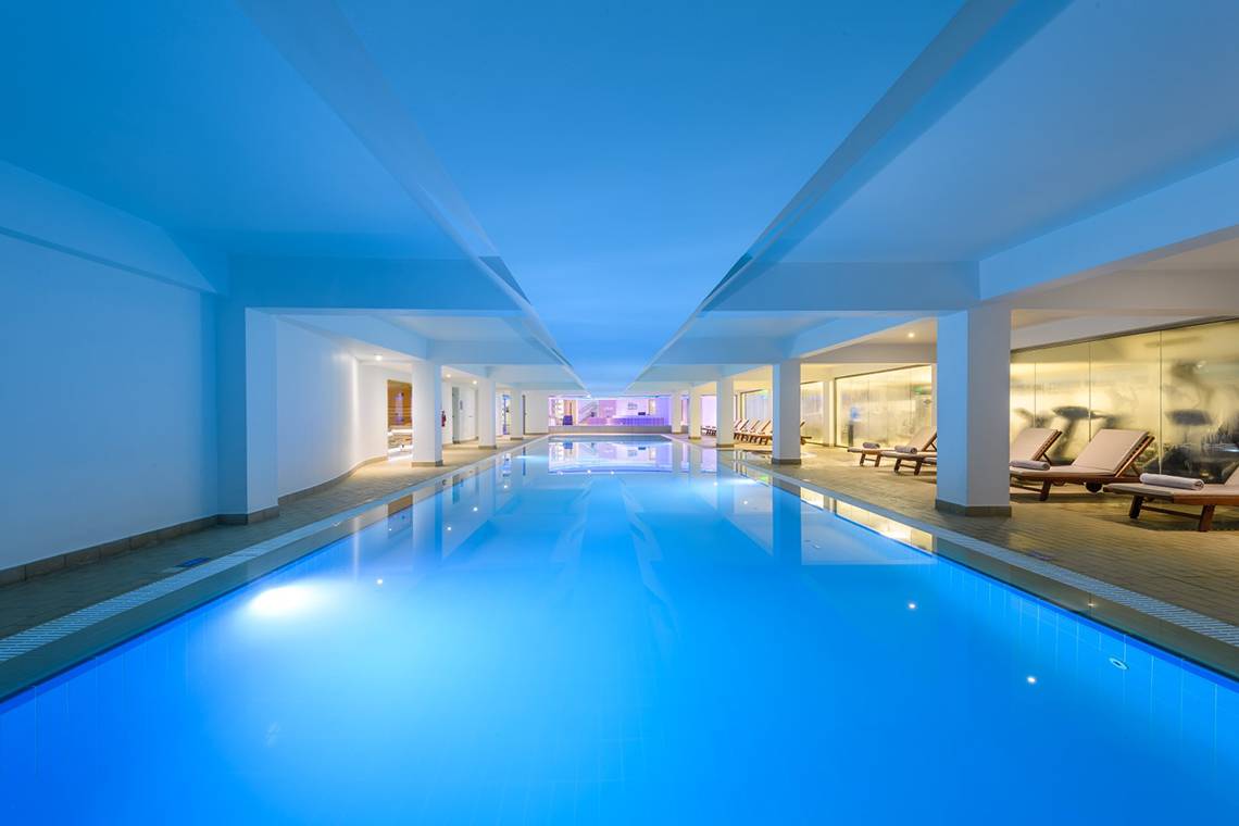 Innenpool im Asterias Beach Hotel mit blauer Beleuchtung und Loungebereich.