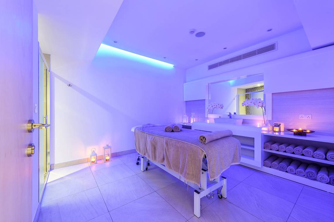 Spa-Behandlungsraum im Asterias Beach Hotel mit violetten Lichtern und einem Behandlungstisch.