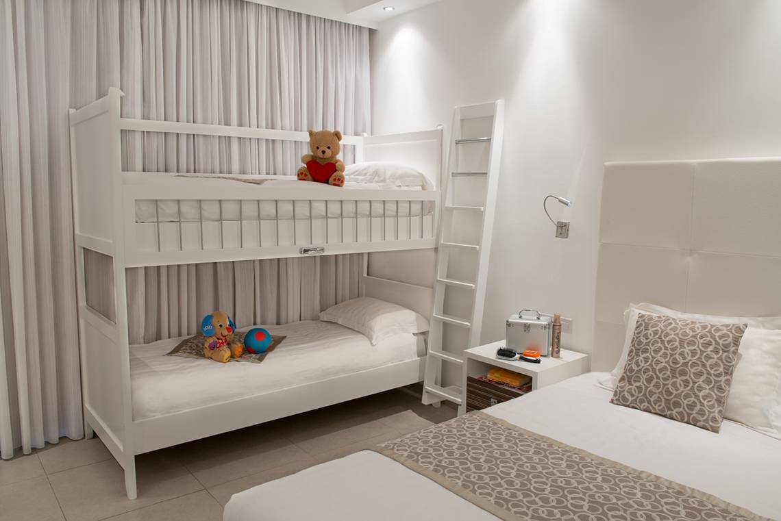 Ein Schlafzimmer mit einem weißen Etagenbett, einem Teddybär und einem Schlafsofa.