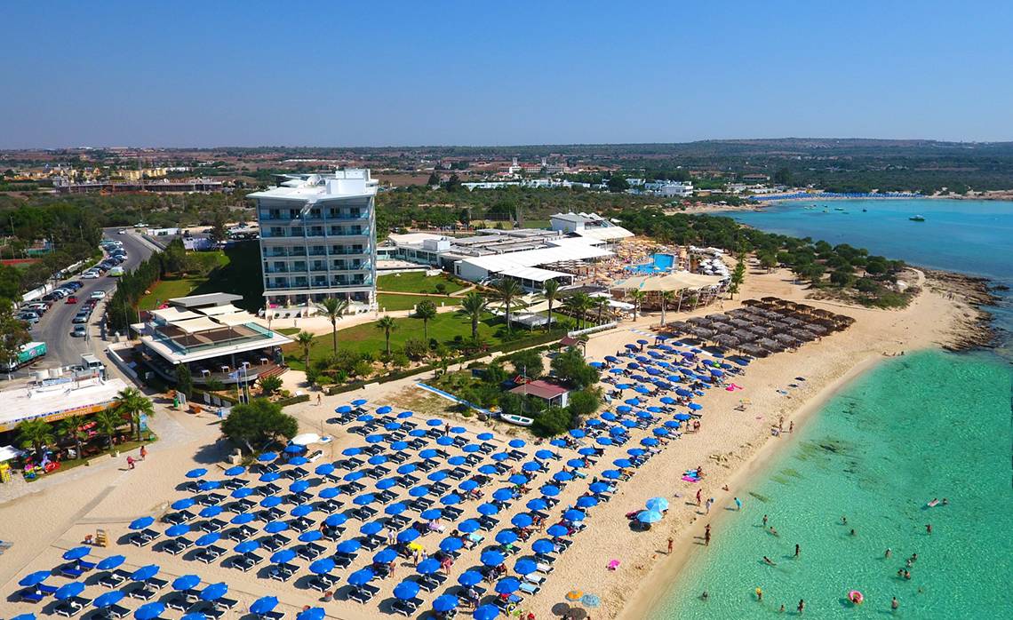 Luftaufnahme des Asterias Beach Hotels mit vielen Liegestühlen und Sonnenschirmen am Strand