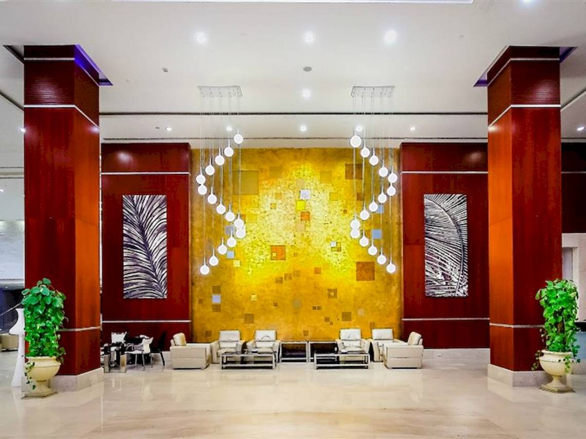 Lobby des Serenity Alma Heights Hotels mit gelber Wand, Kronleuchtern und Möbeln.