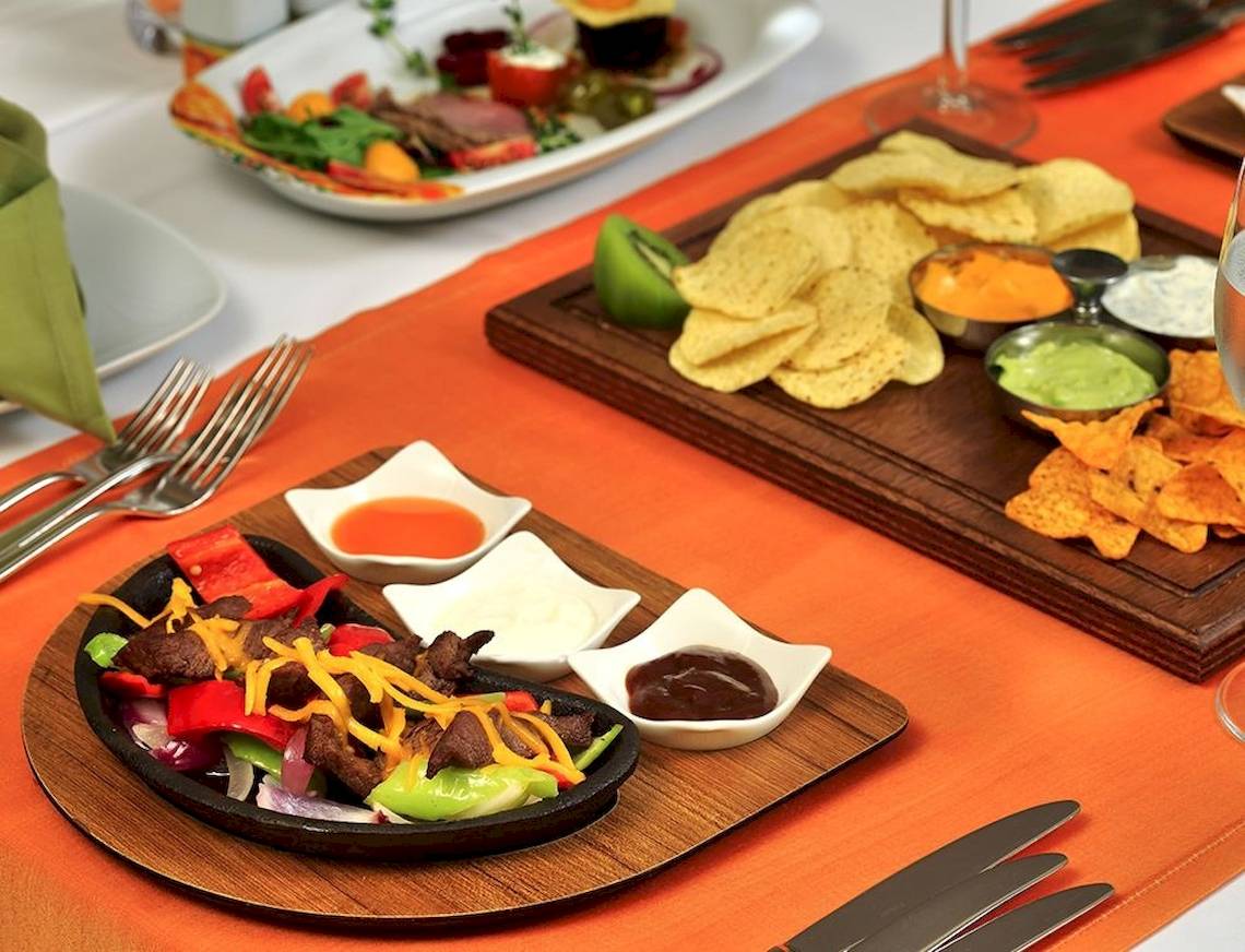 Ein Tisch mit verschiedenen Gerichten und Chips auf einem orangefarbenen Tischtuch.