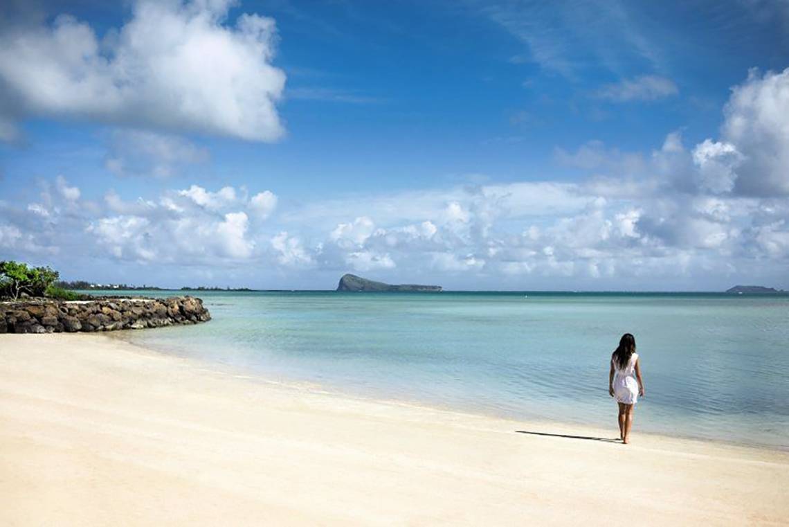 Eine Frau in einem weißen Kleid geht am Strand vor dem Hotel Zilwa Attitude.