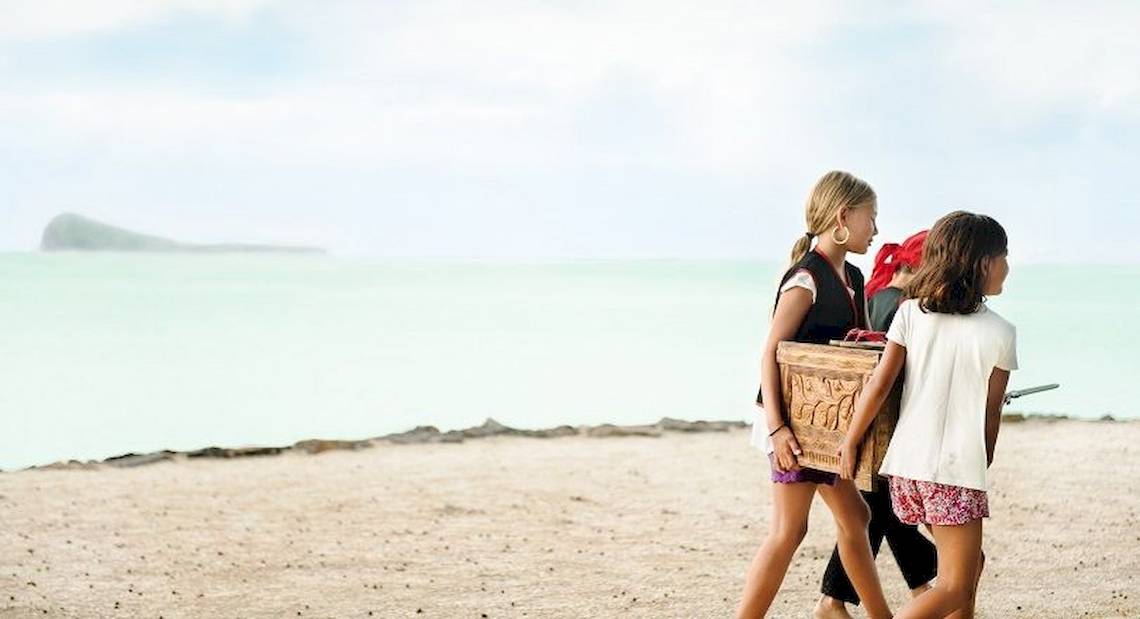 Kinder am Strand tragen Piratenkostüme und tragen einen Holzkasten.