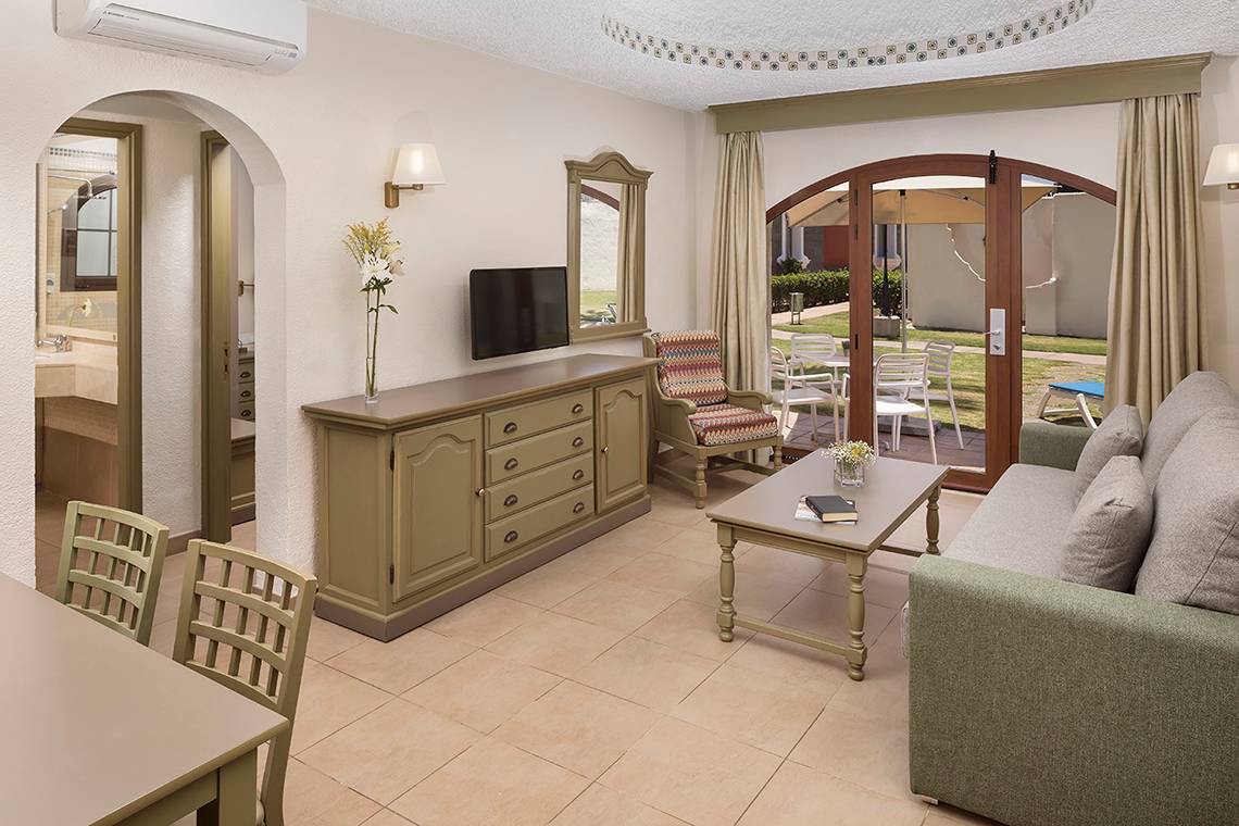 Innenansicht des Wohnbereichs im HD Parque Cristobal Hotel mit Möbeln, Fernseher und offener Terrasse.