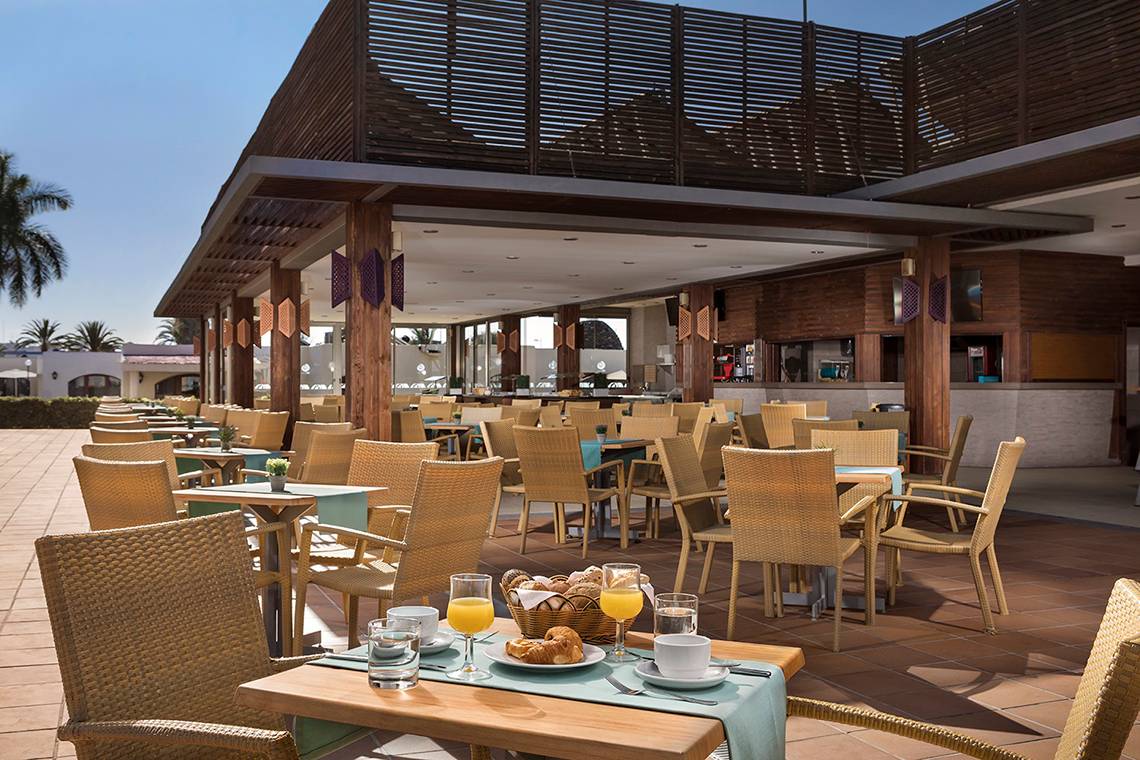 Terrasse des HD Parque Cristobal Hotels mit vollen Tischen und Stühlen, Frühstückskörbe und Getränke auf den Tischen.