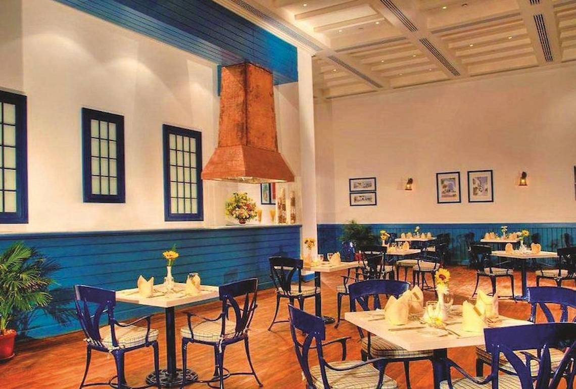 Innenansicht des Restaurants des Jaz Grand Marsa Hotels mit blauen Stühlen und Tischen, einer Theke und einer zentralen Ablufthaube.