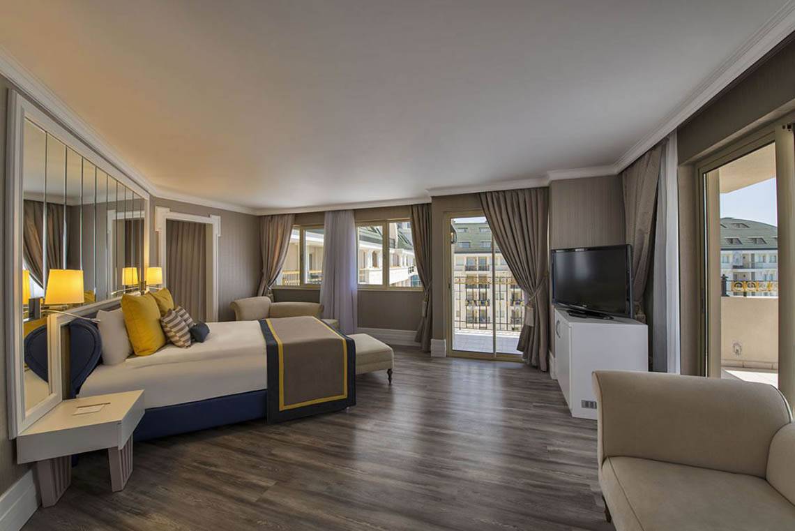 Schlafzimmer im Delphin Diva Premiere Hotel mit großem Bett, Fernseher und Balkonzugang.