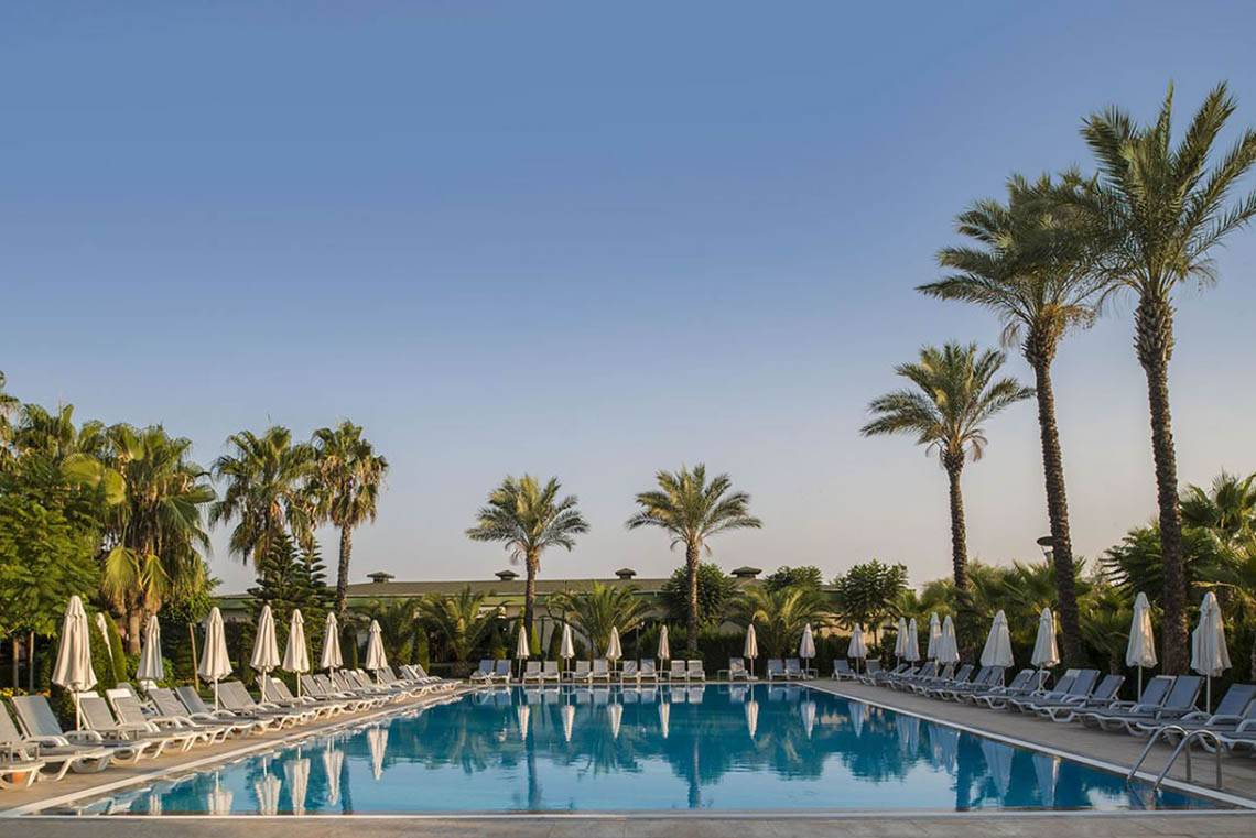Außenpool des Delphin Diva Premiere Hotels mit weißen Sonnenliegen und Sonnenschirmen.