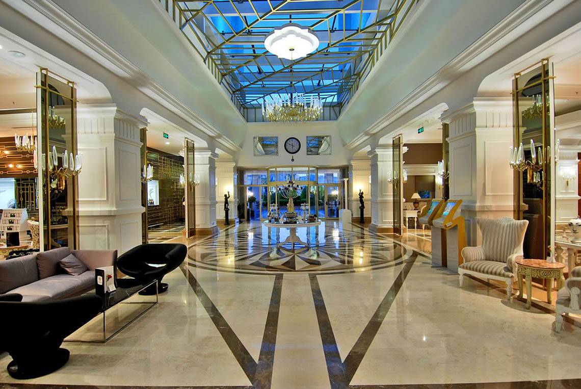 Lobby des Delphin Diva Premiere Hotels mit Marmorboden, Kronleuchtern und Sitzbereichen.