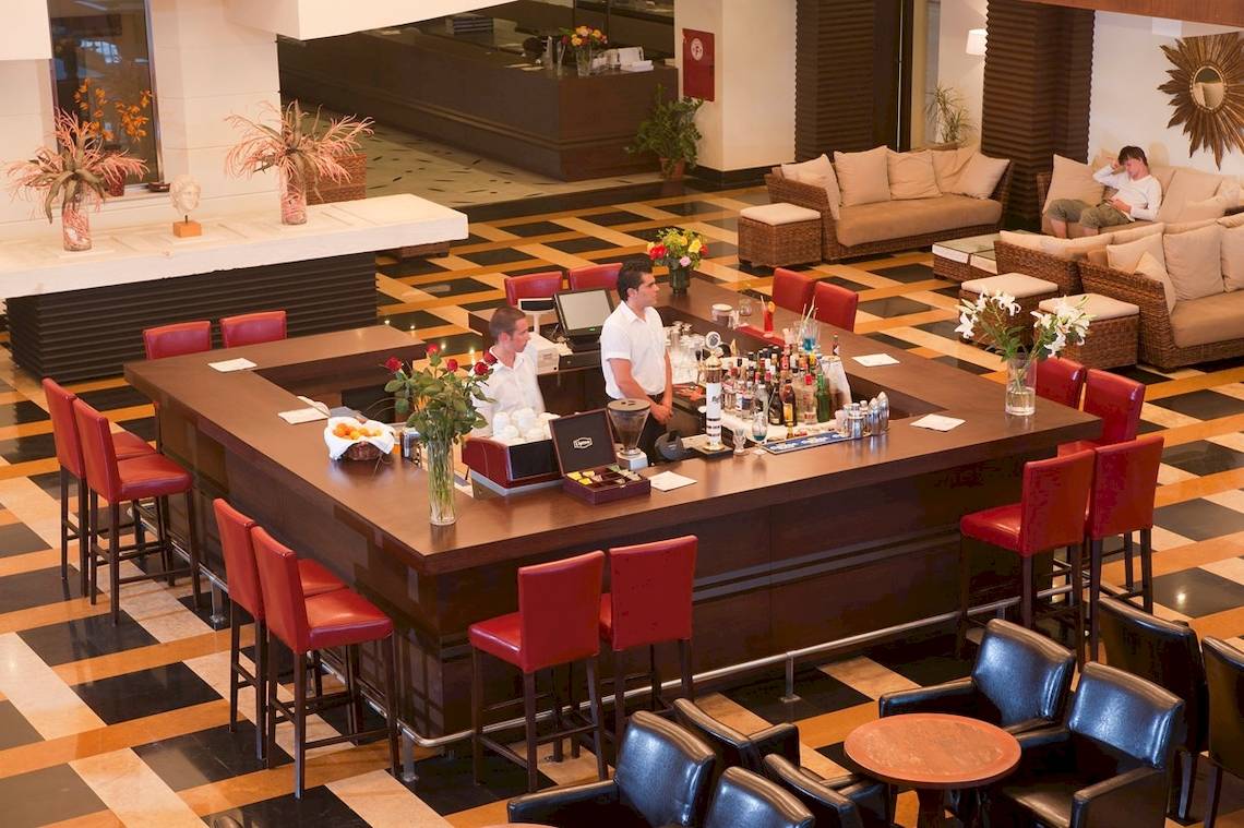 Innenansicht der Bar im Star Beach Village & Water Park mit zwei Barkeepern und roten Stühlen.