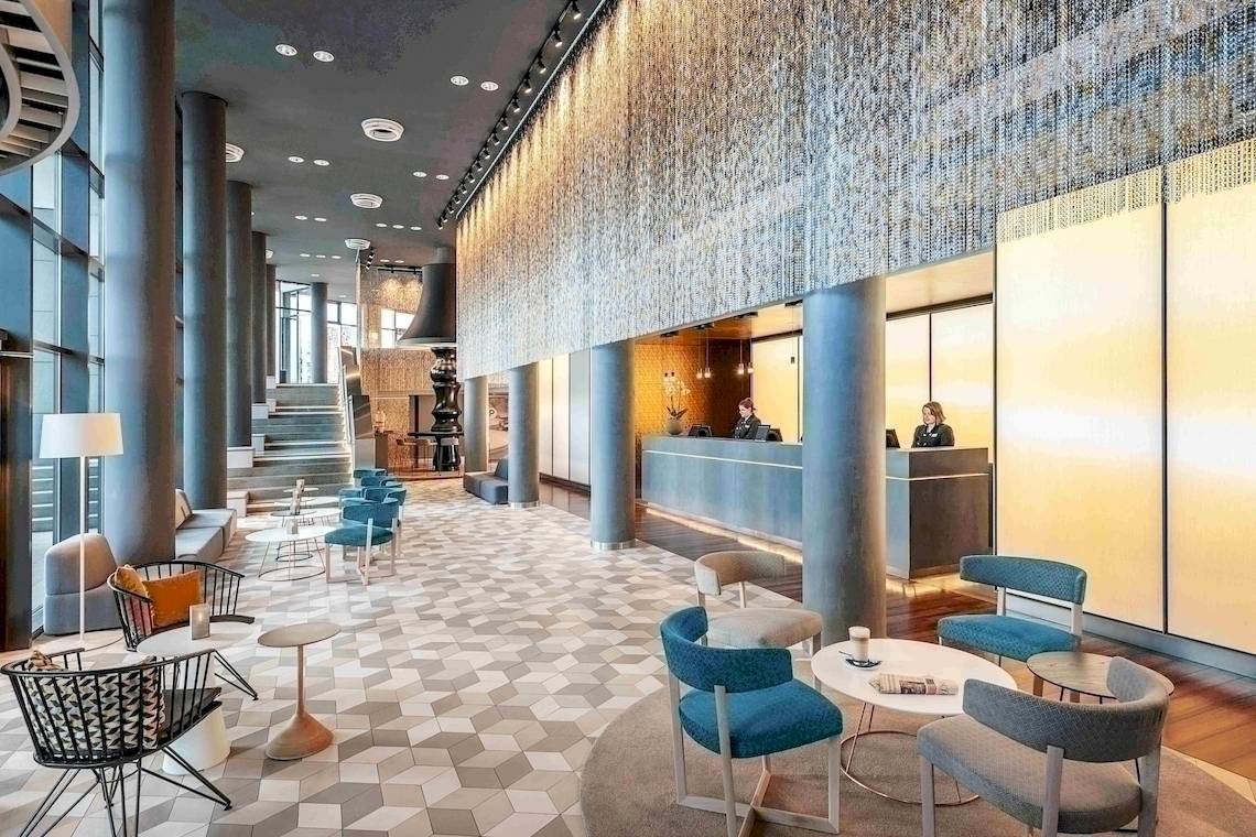 Lobby des NH Berlin Alexanderplatz Hotels mit Rezeption und Sitzbereichen.