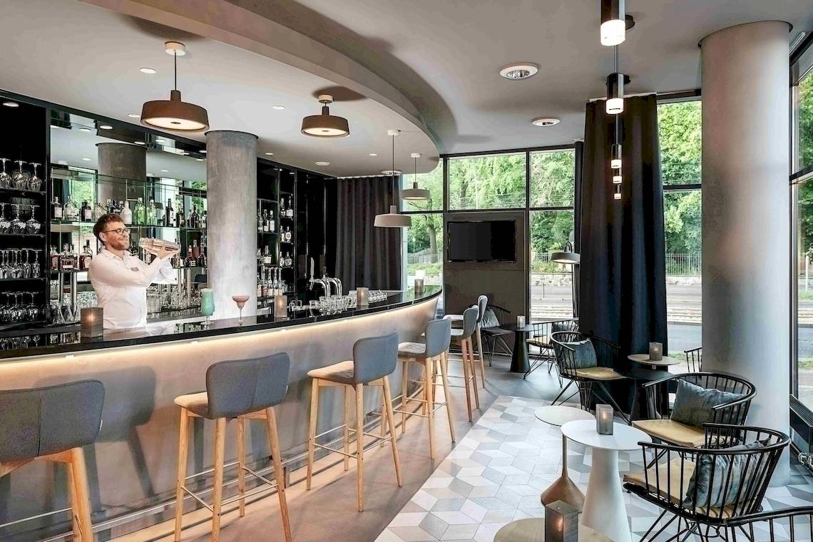 Innenansicht der Bar im NH Berlin Alexanderplatz mit Barkeeper und modernen Möbeln.