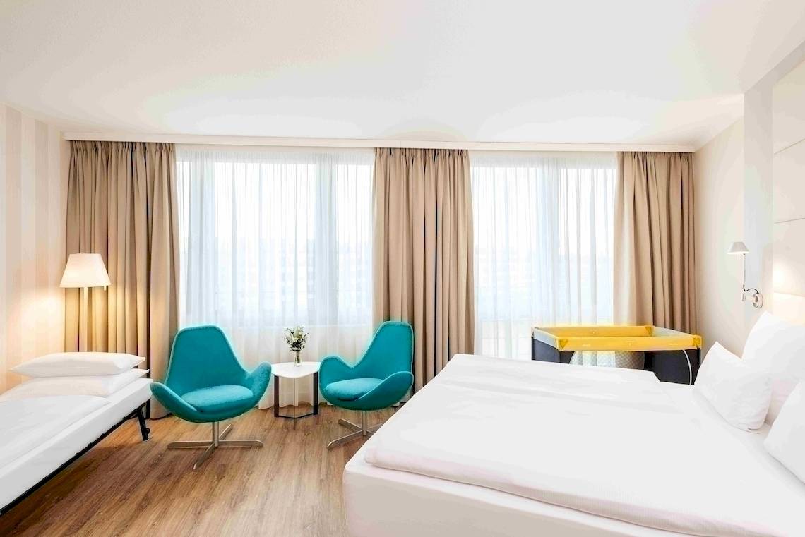 Innenansicht eines Hotelzimmers im NH Berlin Alexanderplatz mit zwei Betten, zwei blauen Stühlen und einem Tisch.