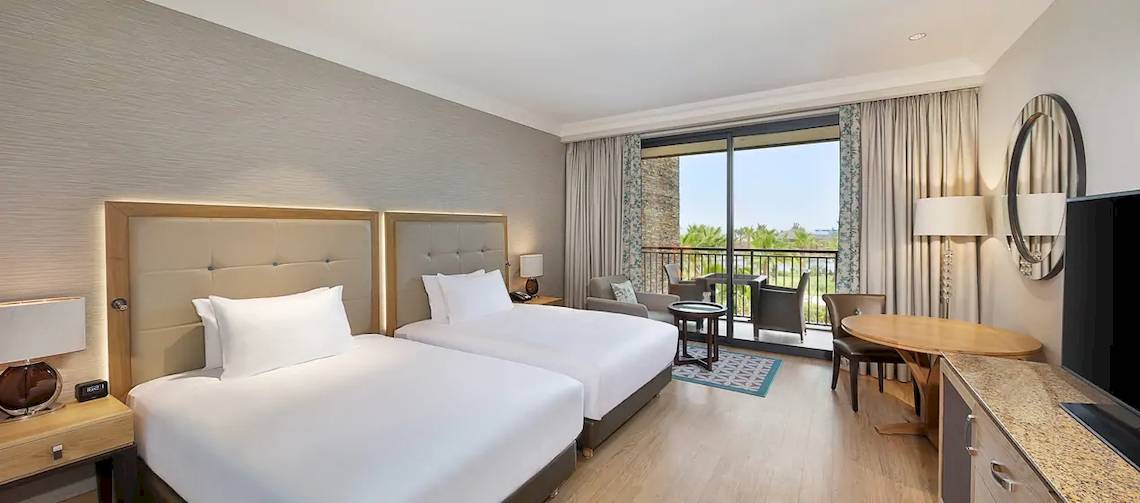 Innenansicht eines Doppelzimmers im Hilton Cabo Verde Sal Resort mit zwei Betten, einem Balkon und modernen Möbeln.