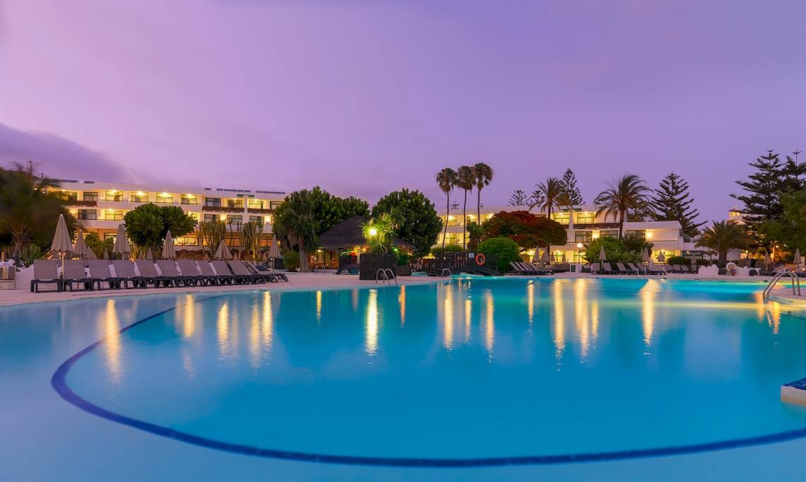 Außenpool des H10 Lanzarote Princess Hotels bei Nacht mit Lounge-Stühlen und Palmen im Hintergrund.