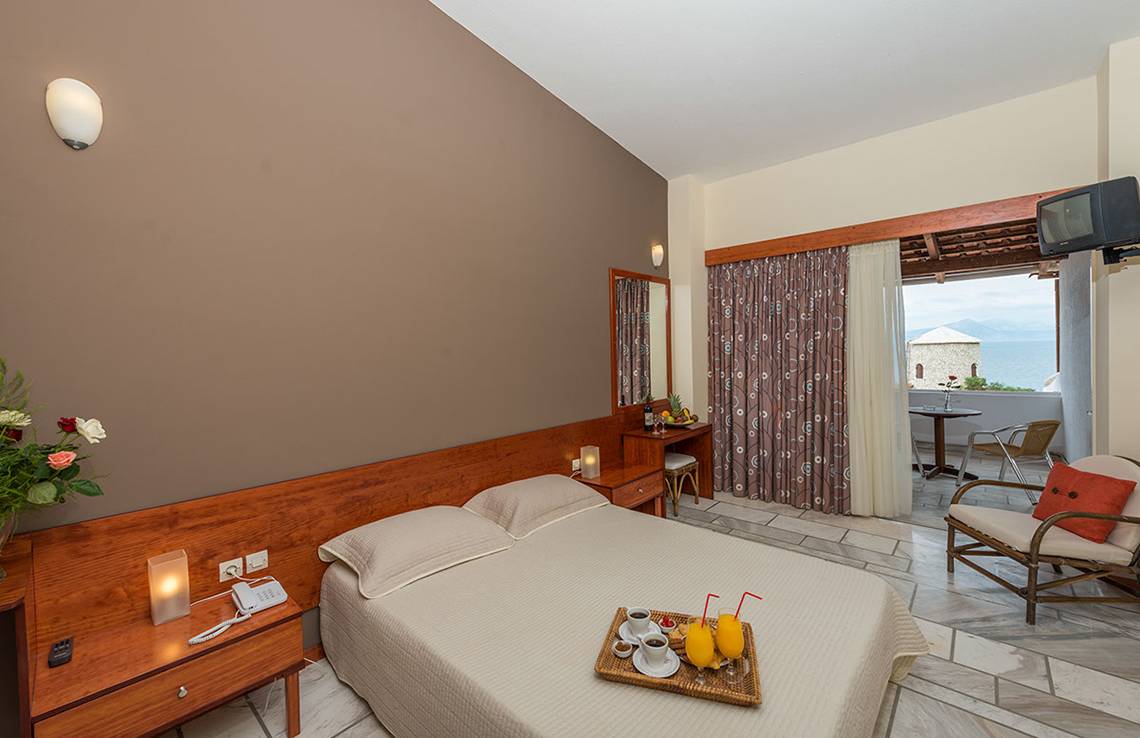 Hotelzimmer im Pavlina Beach Hotel mit Balkon und Meerblick, einschließlich Bett, Frühstückstablett, Tisch und Fernseher.