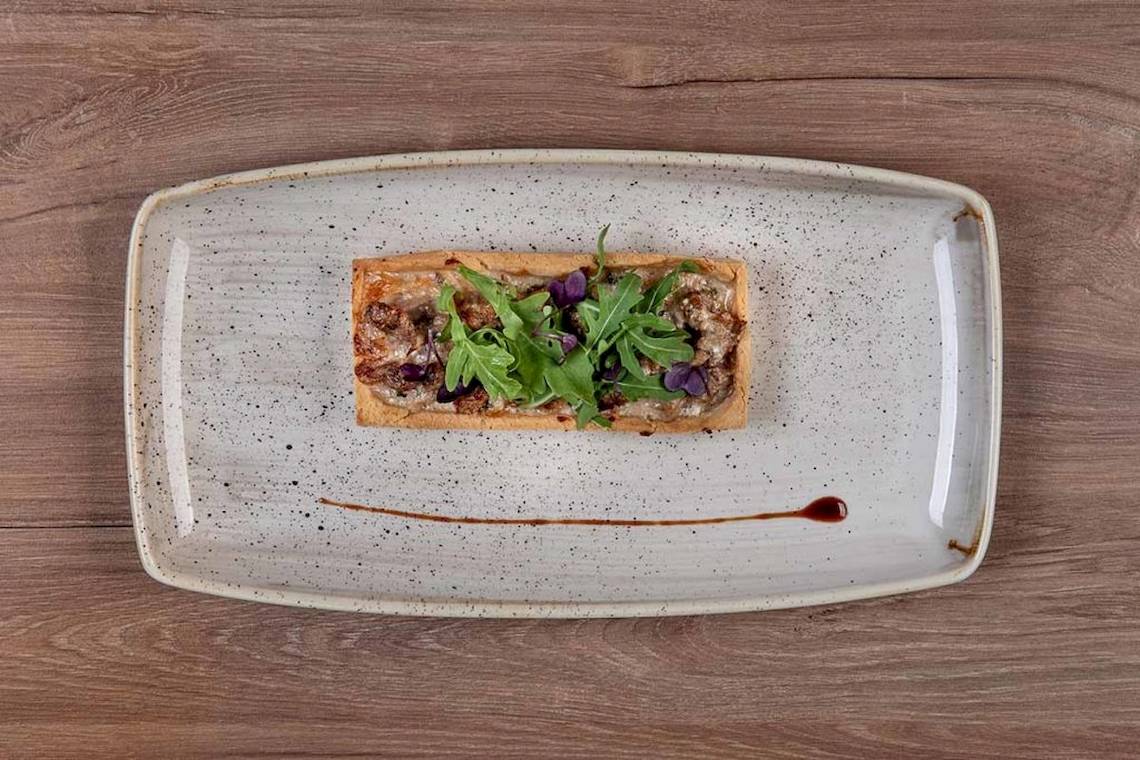 Gebackenes Brot mit Fleisch und Salat auf einem weißen Teller mit schwarzen Punkten auf einem Holztisch.