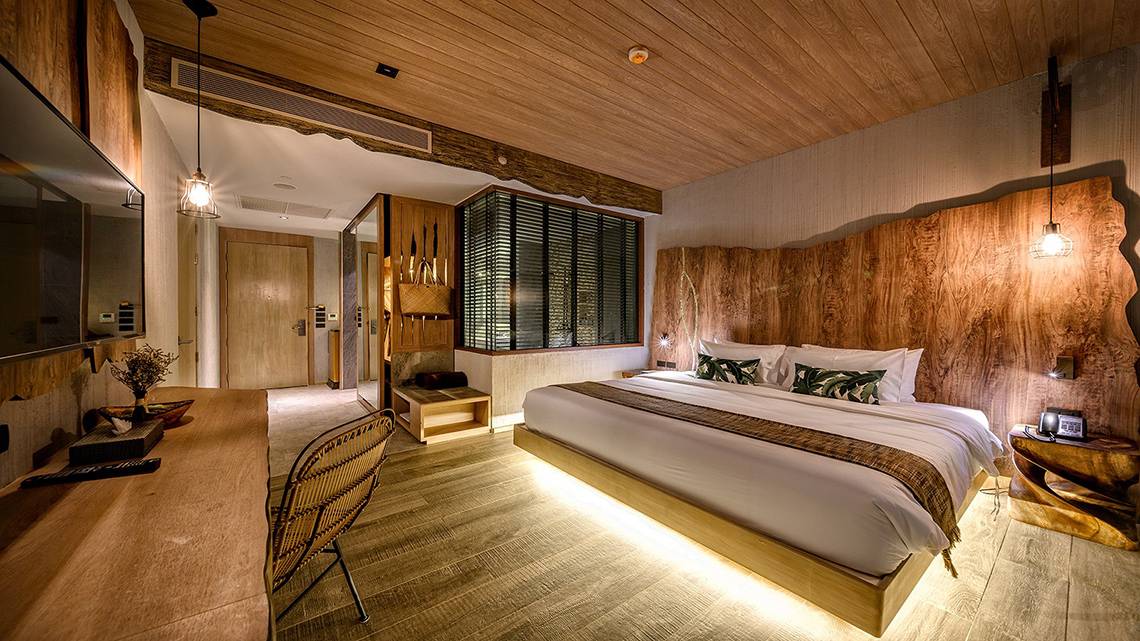 Innenansicht eines Zimmers im Kalima Resort & Villas Khao Lak mit Holzwänden, einem großen Bett und einem Fernseher.