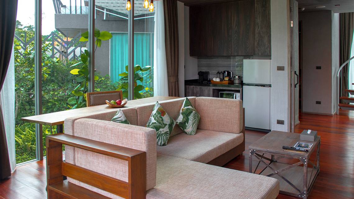 Wohnbereich im Kalima Resort & Villas Khao Lak mit großem Fenster, Couch, Esstisch und Kühlschrank.