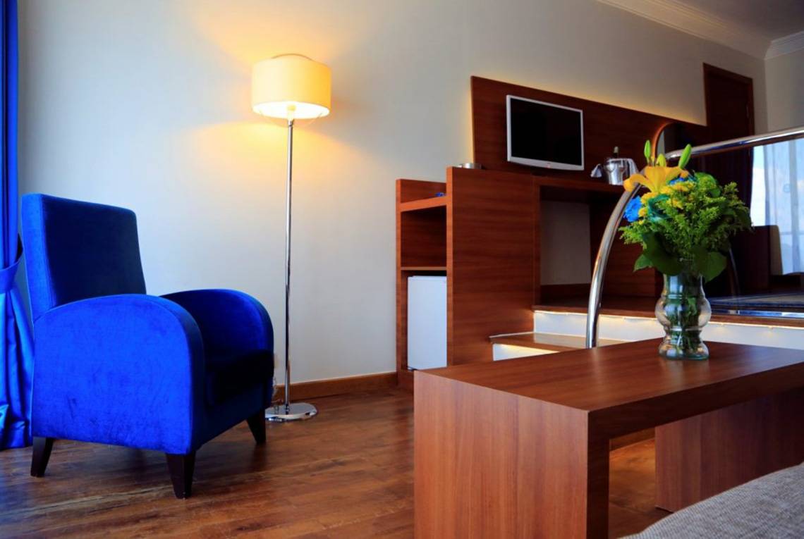 Hotelzimmer im Labranda Ephesus Princess mit blauem Sessel, Lampe und Tisch mit Blumen.