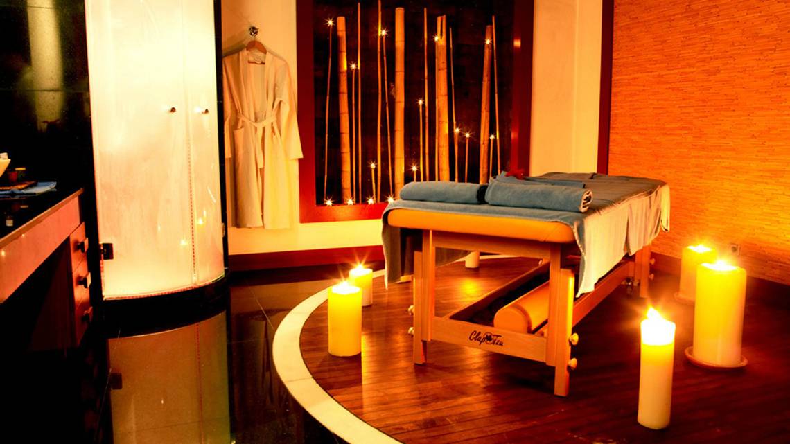 Spa-Behandlungsraum im Kempinski Hotel The Dome Belek mit Massagetisch, blauen Handtüchern und brennenden Kerzen.