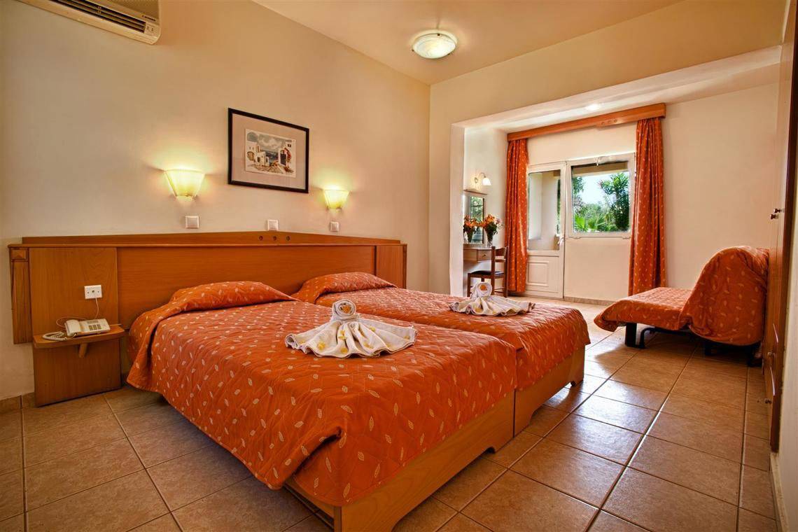 Zwei Betten mit orangen Bettdecken im Hotelzimmer von Ilios K. Village Resort.
