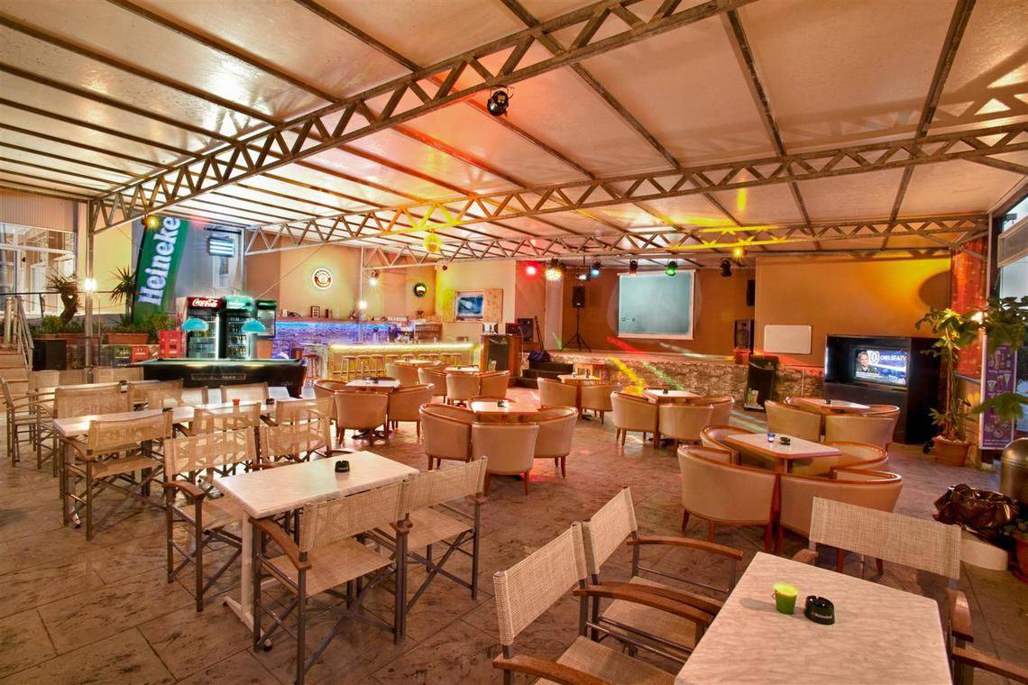 Lounge-Bereich des Ilios K. Village Resorts mit vielen Tischen und Stühlen, Bar und Fernseher.