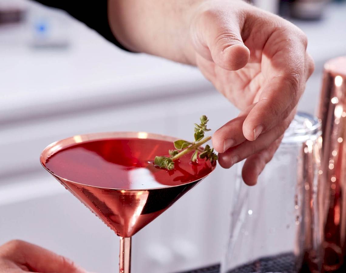 Barkeeper gibt einen Cocktail mit Thymian einhändig in ein Glas.