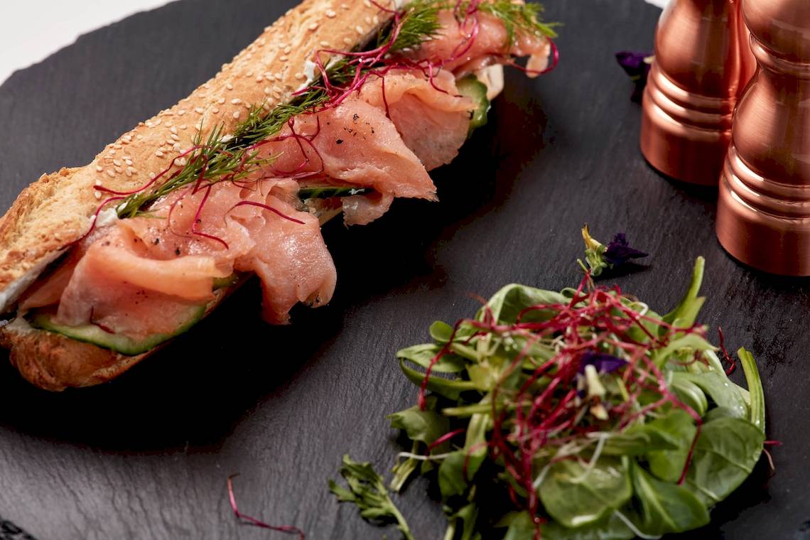 Ein Lachssandwich mit Salat auf einem schwarzen Teller.