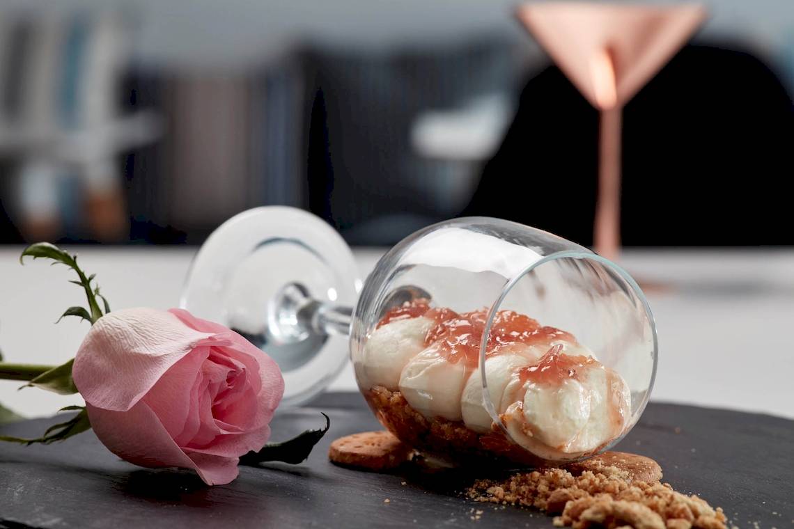 Dessert im Glas mit Karamellsauce und Rose neben einem halbvollen Glas
